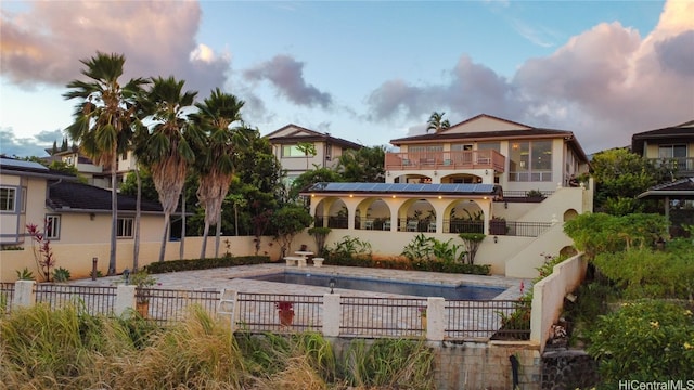 back house at dusk featuring a fenced in pool and a balcony