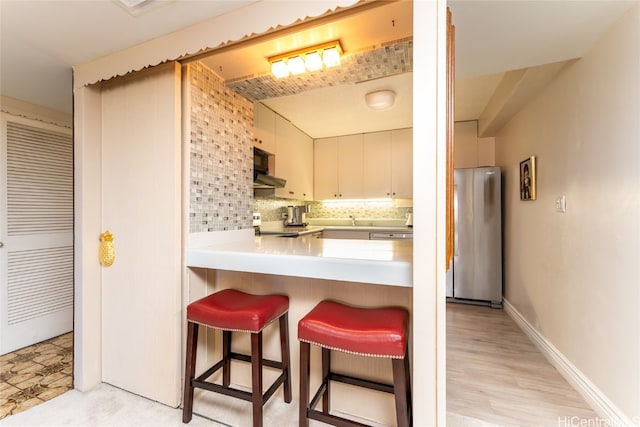 kitchen featuring a breakfast bar area, kitchen peninsula, stainless steel appliances, light wood-type flooring, and tasteful backsplash