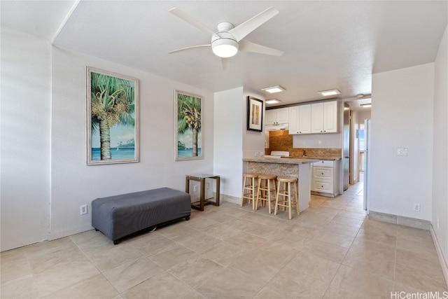 kitchen featuring a breakfast bar, white cabinetry, light tile patterned floors, ceiling fan, and kitchen peninsula