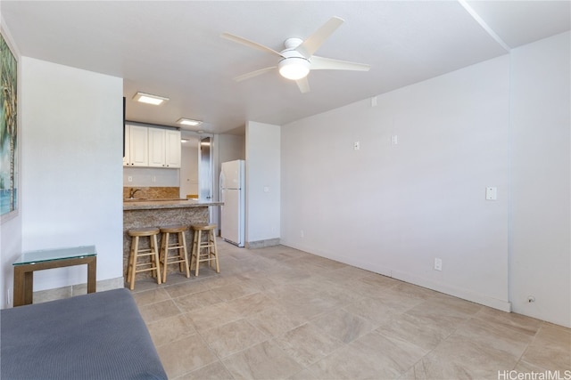 kitchen featuring ceiling fan, white refrigerator, white cabinets, a kitchen bar, and kitchen peninsula