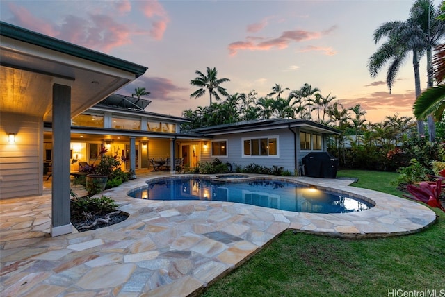 pool at dusk with a patio, area for grilling, and a lawn