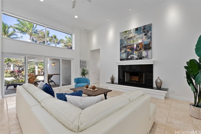 living room with a high ceiling, ornamental molding, light tile patterned floors, a fireplace, and ceiling fan