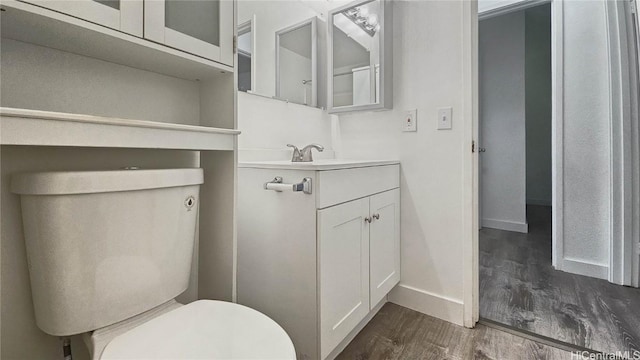 half bath featuring baseboards, vanity, toilet, and wood finished floors