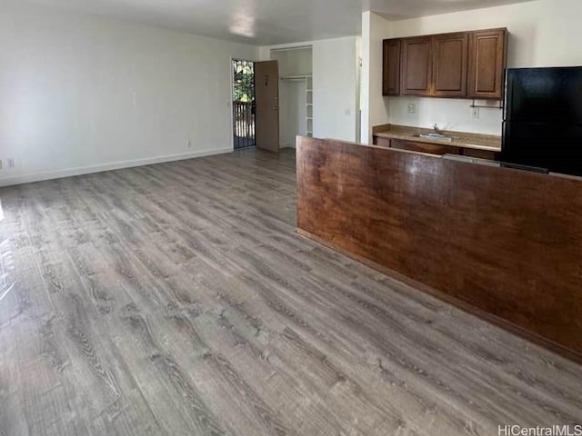 kitchen featuring light wood-style floors, freestanding refrigerator, open floor plan, a sink, and baseboards