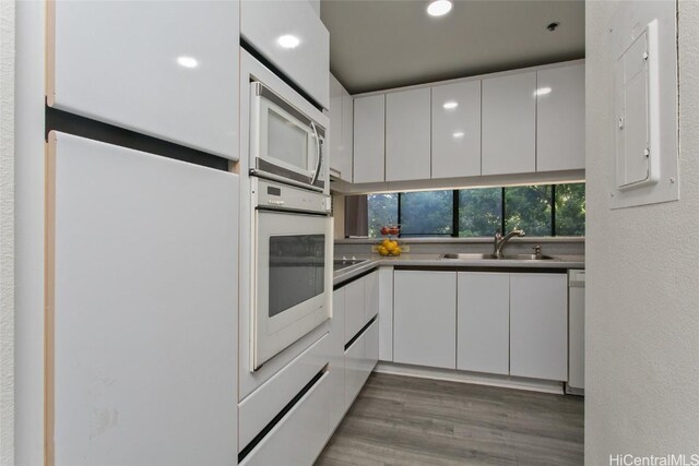 kitchen featuring white appliances, sink, white cabinets, hardwood / wood-style flooring, and electric panel