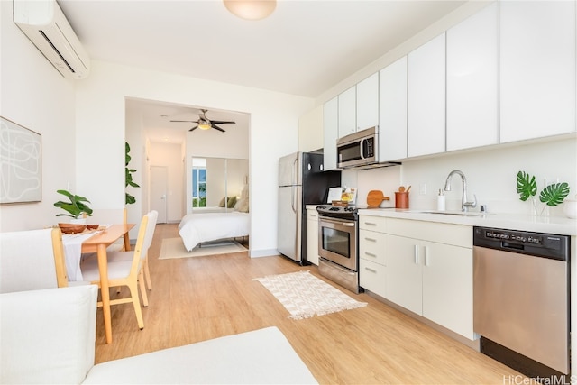 kitchen featuring an AC wall unit, appliances with stainless steel finishes, sink, and white cabinets