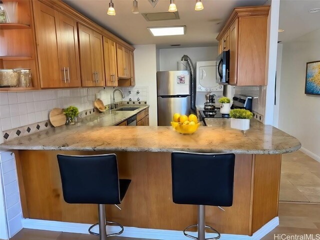 kitchen featuring kitchen peninsula, stainless steel appliances, a breakfast bar, backsplash, and sink