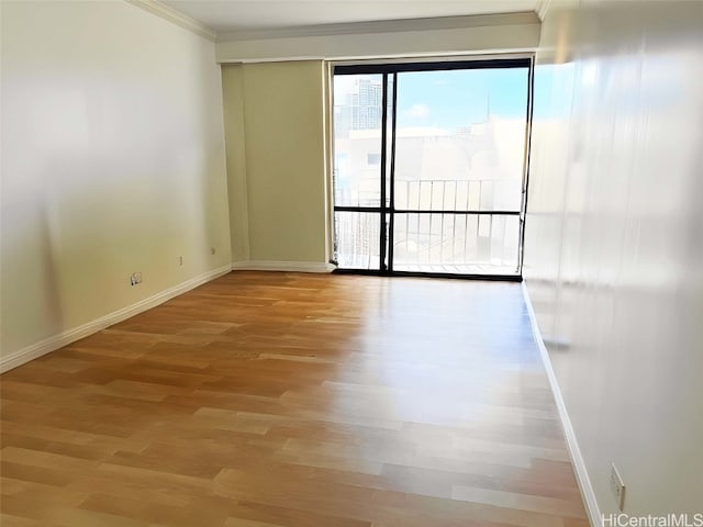 empty room with light wood-type flooring, baseboards, and ornamental molding