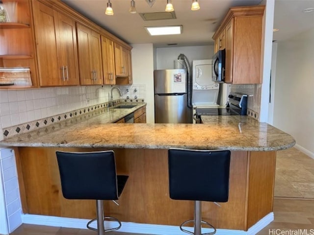 kitchen with a sink, open shelves, light stone counters, stainless steel appliances, and a peninsula