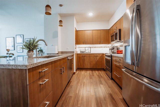 kitchen featuring kitchen peninsula, hanging light fixtures, light wood-type flooring, sink, and stainless steel appliances