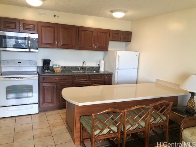 kitchen featuring a kitchen breakfast bar, sink, light tile patterned floors, a textured ceiling, and white appliances