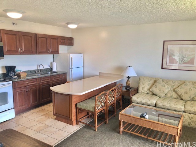 kitchen with a textured ceiling, sink, light tile patterned floors, and white appliances