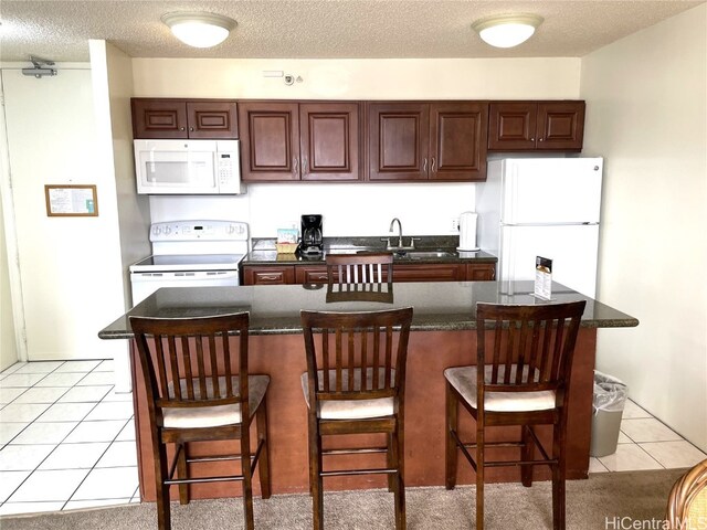 kitchen featuring sink, a kitchen bar, light tile patterned floors, a textured ceiling, and white appliances