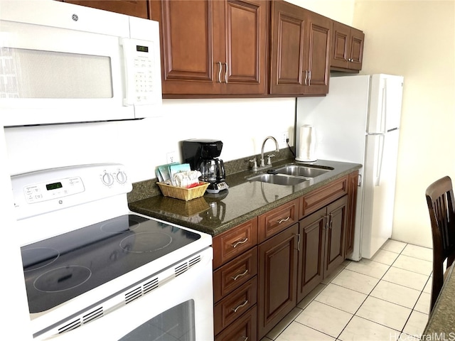 kitchen featuring white appliances, light tile patterned floors, dark stone countertops, and sink