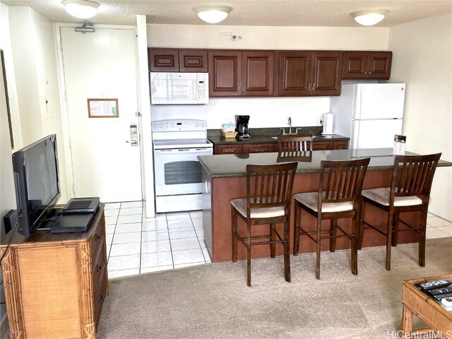 kitchen with a kitchen breakfast bar, a textured ceiling, light colored carpet, and white appliances