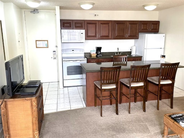 kitchen featuring a kitchen island, a breakfast bar, sink, light tile patterned floors, and white appliances