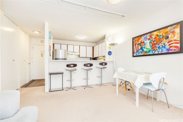 kitchen featuring white cabinets, a textured ceiling, light colored carpet, and stainless steel refrigerator