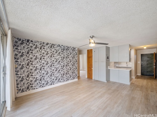 unfurnished living room featuring sink, light hardwood / wood-style flooring, a textured ceiling, and ceiling fan