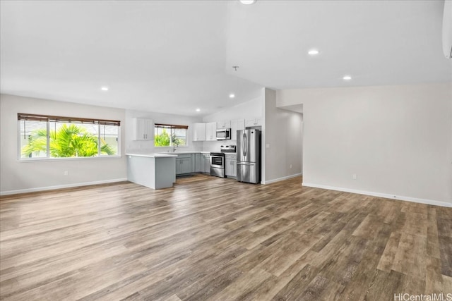 unfurnished living room with sink, vaulted ceiling, and light hardwood / wood-style flooring