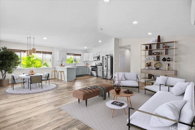 living room with sink, light hardwood / wood-style floors, and vaulted ceiling