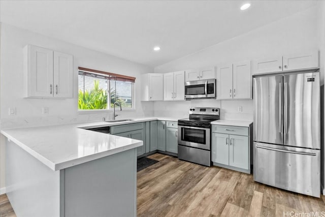 kitchen featuring lofted ceiling, kitchen peninsula, sink, appliances with stainless steel finishes, and light hardwood / wood-style floors