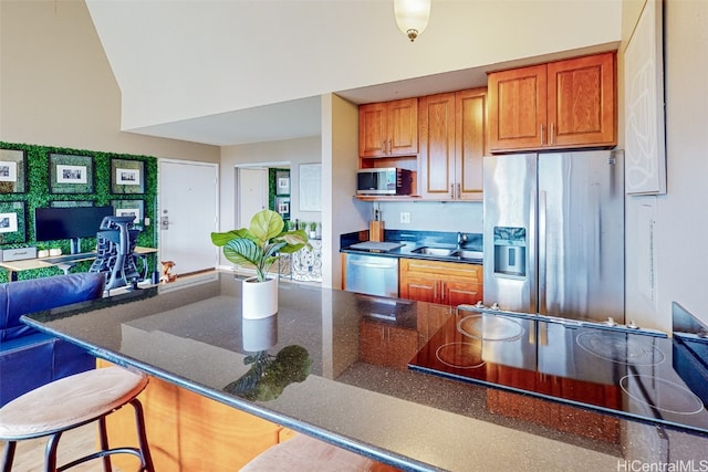 kitchen with appliances with stainless steel finishes, sink, a kitchen bar, vaulted ceiling, and dark stone countertops