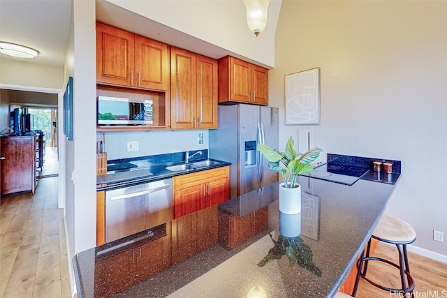 kitchen featuring a breakfast bar area, stainless steel appliances, dark stone counters, sink, and light wood-type flooring