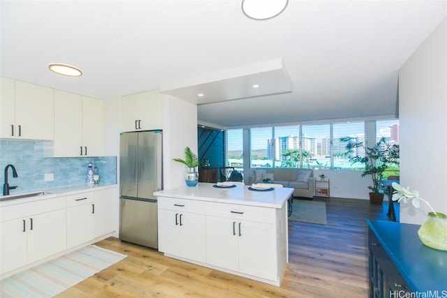 kitchen featuring sink, light wood-type flooring, stainless steel fridge, white cabinets, and decorative backsplash