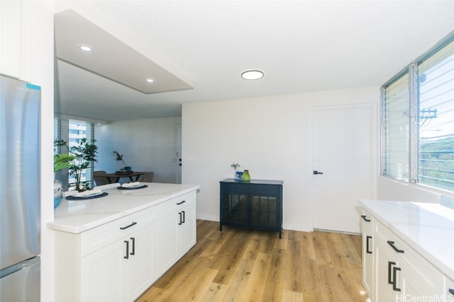 kitchen with white cabinets, light hardwood / wood-style floors, light stone countertops, and stainless steel fridge