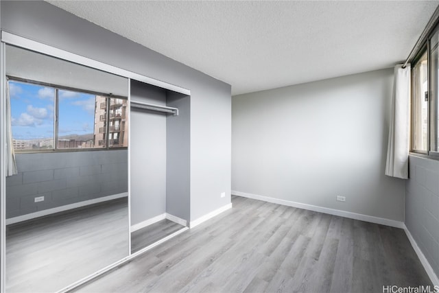 unfurnished bedroom with baseboards, concrete block wall, wood finished floors, and a textured ceiling