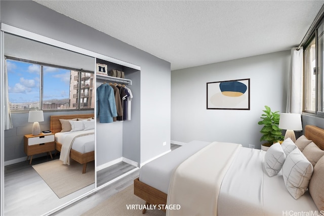 bedroom with a textured ceiling, multiple windows, wood finished floors, and baseboards