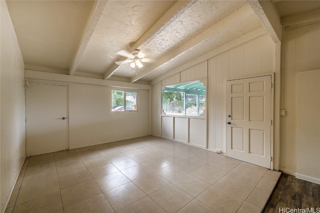 tiled spare room featuring wooden walls, lofted ceiling with beams, and ceiling fan