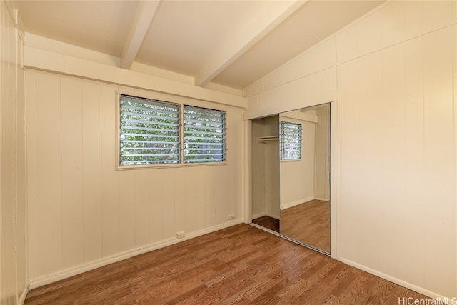 unfurnished bedroom with vaulted ceiling with beams, a closet, wooden walls, and wood-type flooring