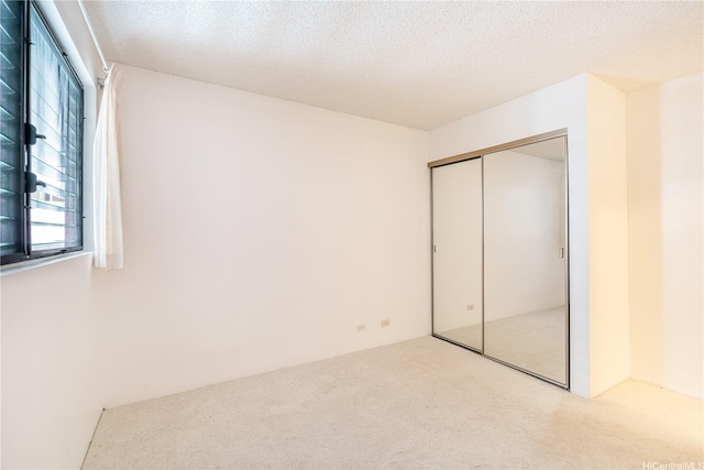 unfurnished bedroom featuring light colored carpet, a closet, and a textured ceiling