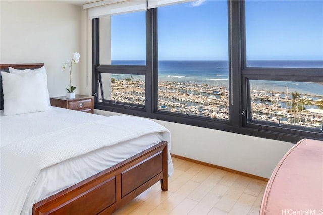 bedroom with light wood finished floors, a water view, and baseboards