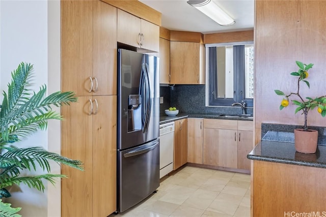 kitchen featuring stainless steel fridge, dark stone counters, dishwasher, decorative backsplash, and a sink