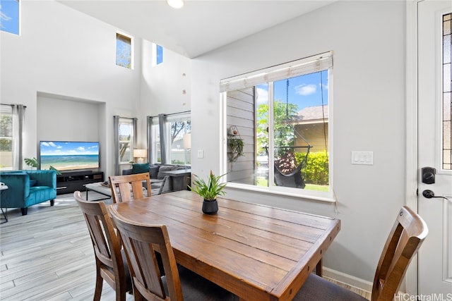 dining space featuring light hardwood / wood-style floors, a wealth of natural light, and a high ceiling