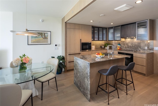 kitchen with light wood finished floors, black appliances, a breakfast bar area, backsplash, and recessed lighting