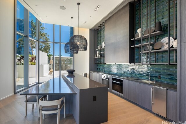 kitchen featuring hanging light fixtures, stainless steel appliances, a wall of windows, decorative backsplash, and light hardwood / wood-style flooring