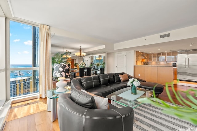 living room with expansive windows, a water view, a chandelier, and light hardwood / wood-style flooring