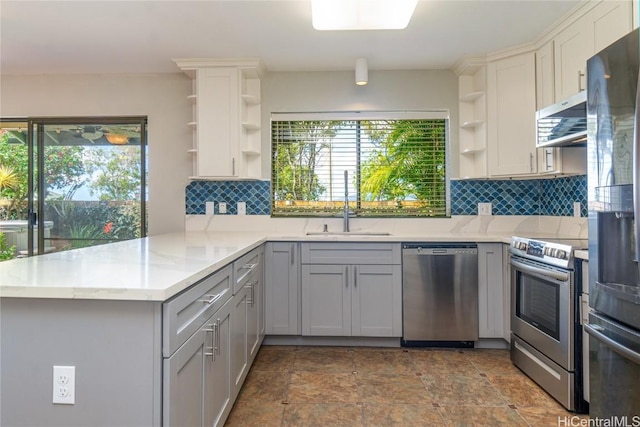 kitchen featuring a peninsula, stainless steel appliances, gray cabinetry, open shelves, and a sink