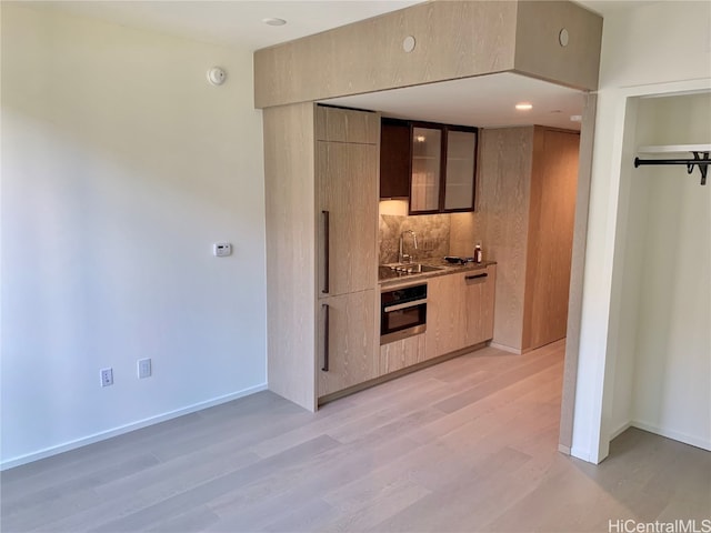 kitchen featuring light hardwood / wood-style flooring, sink, oven, and backsplash