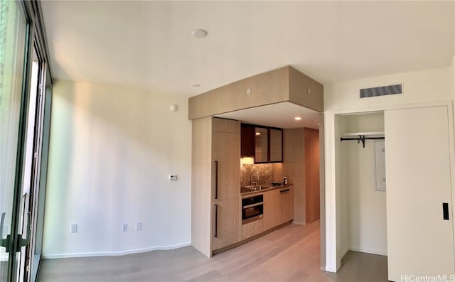 kitchen featuring tasteful backsplash, sink, stainless steel oven, and light hardwood / wood-style flooring