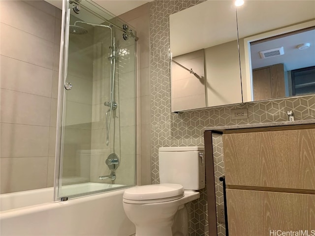 bathroom with tile walls, bath / shower combo with glass door, toilet, and backsplash