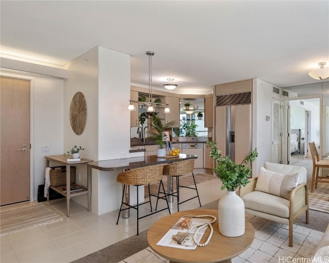 kitchen with a breakfast bar, hanging light fixtures, built in refrigerator, light tile patterned floors, and kitchen peninsula