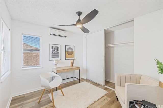 sitting room featuring ceiling fan, light hardwood / wood-style floors, an AC wall unit, and a textured ceiling