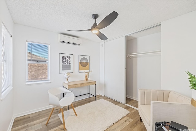 sitting room featuring an AC wall unit, a textured ceiling, ceiling fan, light wood-style flooring, and baseboards