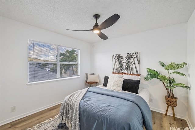 bedroom with ceiling fan, wood-type flooring, and a textured ceiling