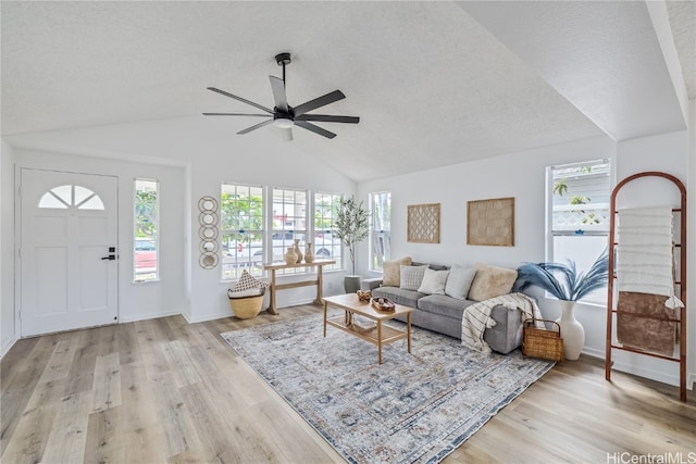 living room with a wealth of natural light, ceiling fan, light hardwood / wood-style floors, and vaulted ceiling