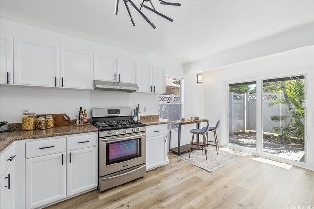 kitchen with white cabinets, light wood finished floors, dark stone countertops, gas stove, and under cabinet range hood